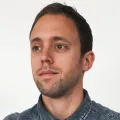 Man with short brown hair and beard, wearing a blue button-up shirt, looking slightly left.
