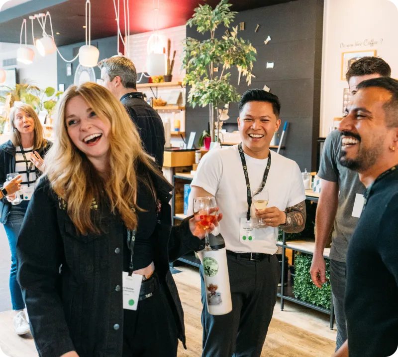 Group of people smiling and chatting casually while holding drinks in a modern indoor space.