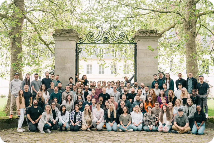 Large diverse group of people posing outdoors under a decorative gate with trees in the background.