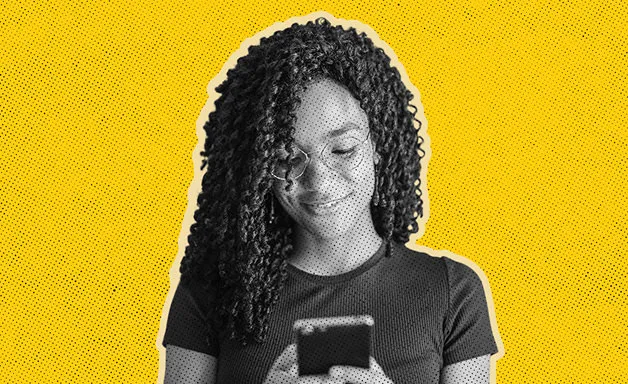 Smiling woman with curly hair looking at her smartphone on a yellow background.