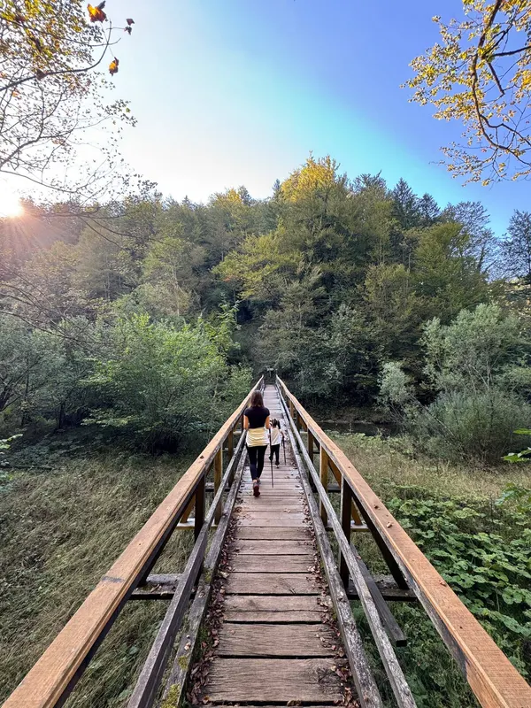 A teammate and her young daughter walking across a wooden footbridge into an autumn forest