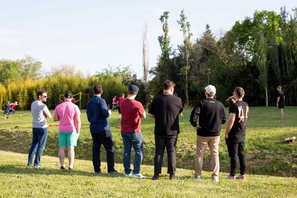 A row of teammates seen from behind, watching a pickup soccer game on the grass